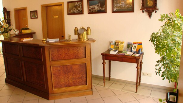 Un comptoir d’accueil avec un revêtement en bois, une horloge, des tableaux encadrés accrochés au mur et une petite table avec des brochures.
