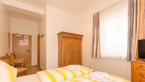 A hotel room with two beds, a wooden wardrobe, a television, and a window with curtains.