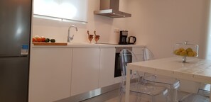 A modern kitchen with white cabinets, a stainless steel refrigerator, a built-in dishwasher, a coffee maker, and a glass fruit bowl on the counter. - Modern House near Parikia with 3 bedrooms & 2 bath (Πάρος)