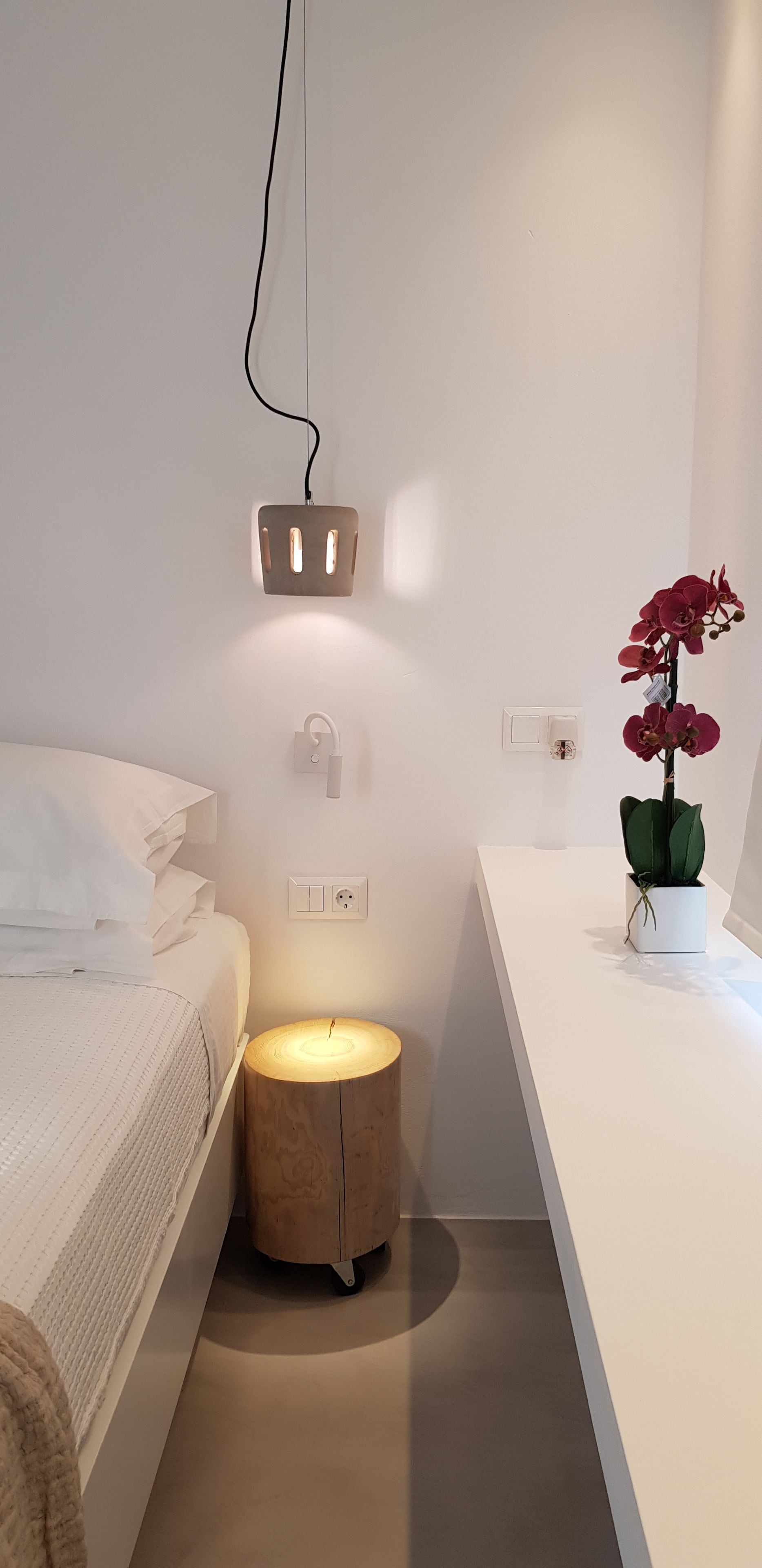 A modern bedroom with a bed, bedside table, nightstand, and a potted orchid.