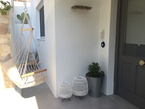 A white exterior wall with a macrame hanging chair, two white wicker stools, and a potted plant near a door. - Modern House near Parikia with 3 bedrooms & 2 bath (Πάρος)