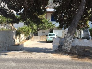 A residential street with a parked car, trees, and a building with a blue door in the background. - Modern House near Parikia with 3 bedrooms & 2 bath (Πάρος)
