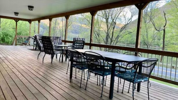 Uma área externa coberta com deck de madeira, cadeiras de metal e uma mesa.