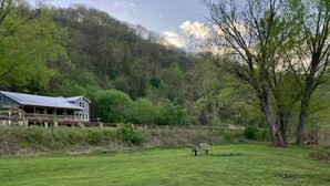 Uma casa grande com varanda, cercada por um campo gramado e árvores.