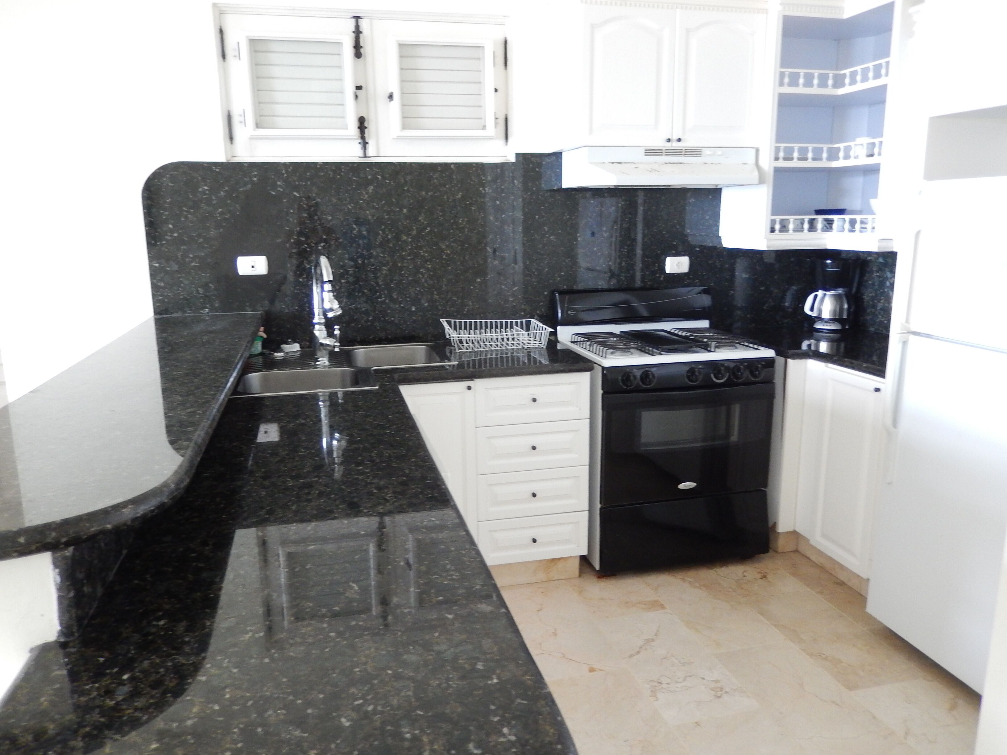 A compact kitchen with a black countertop, white cabinets, a stove, and a coffee maker.