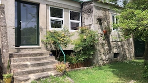 A stone building with a set of stone steps leading to a door, surrounded by greenery and a small garden area.