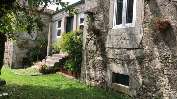 Um edifício de pedra com uma escadaria que leva a uma porta, rodeado por vegetação.
