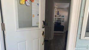 A white door with a glass panel, a doormat with a tropical design, and a teal chair outside.