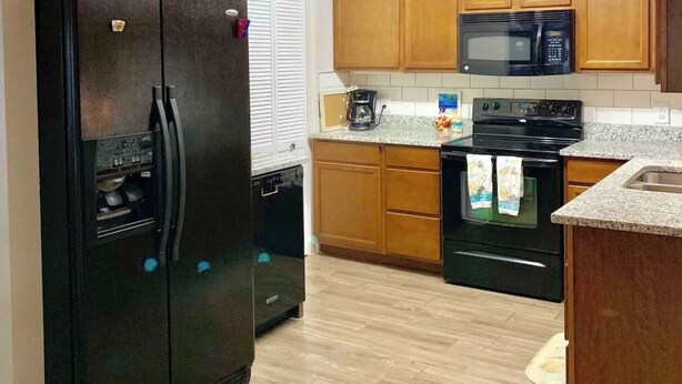 A kitchen with wooden cabinets, a black refrigerator, a microwave, and a stove.