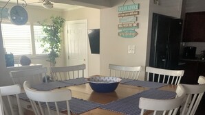 A dining area with a wooden table and white chairs, a blue bowl, and a wall sign with nautical-themed text.