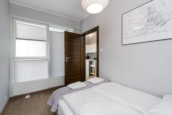 Een slaapkamer met een bed, een raam met zonwering, een deur naar een badkamer en een kunstwerk aan de muur.