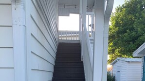 A set of dark wooden stairs leading up to a white porch with a railing.