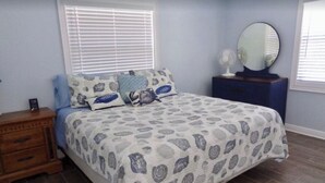 A bedroom with a bed, a dresser, a mirror, and a window with blinds.
