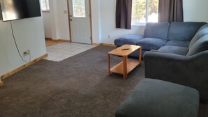 Un salon avec un canapé gris, une table basse en bois et un téléviseur à écran plat fixé au mur.