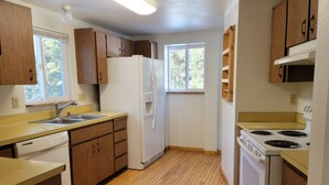 Une cuisine avec des meubles de rangement en bois, un réfrigérateur blanc, une cuisinière et un lave-vaisselle.