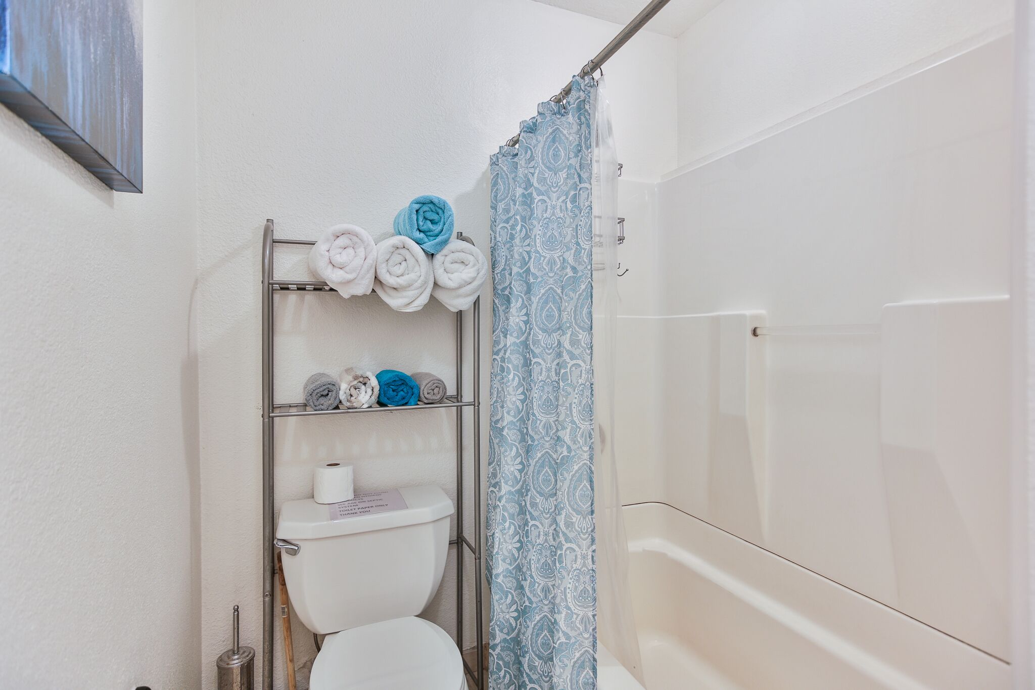 Ein Badezimmer mit Toilette, Handtuchhalter mit Handtüchern, einer Duschvorhang und einem Metallregal.