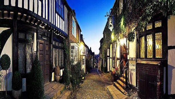 Une rue pavée bordée de bâtiments traditionnels à colombages, dont certains arborent des enseignes bien visibles.