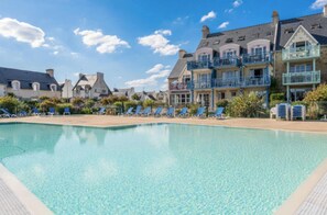 Una piscina con sillones de descanso y varias casas al fondo.