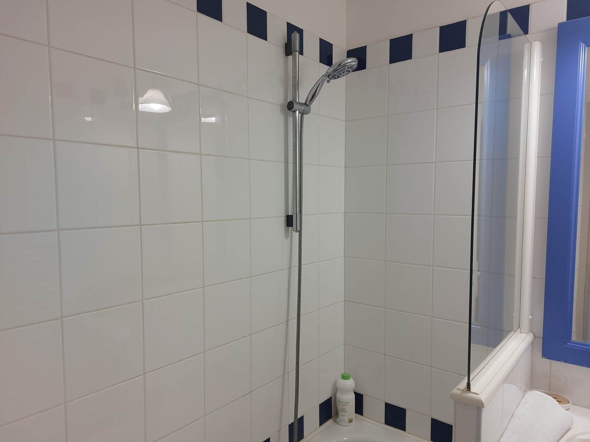 Une salle de bain avec des carreaux blancs, une douche, un lavabo et un miroir.