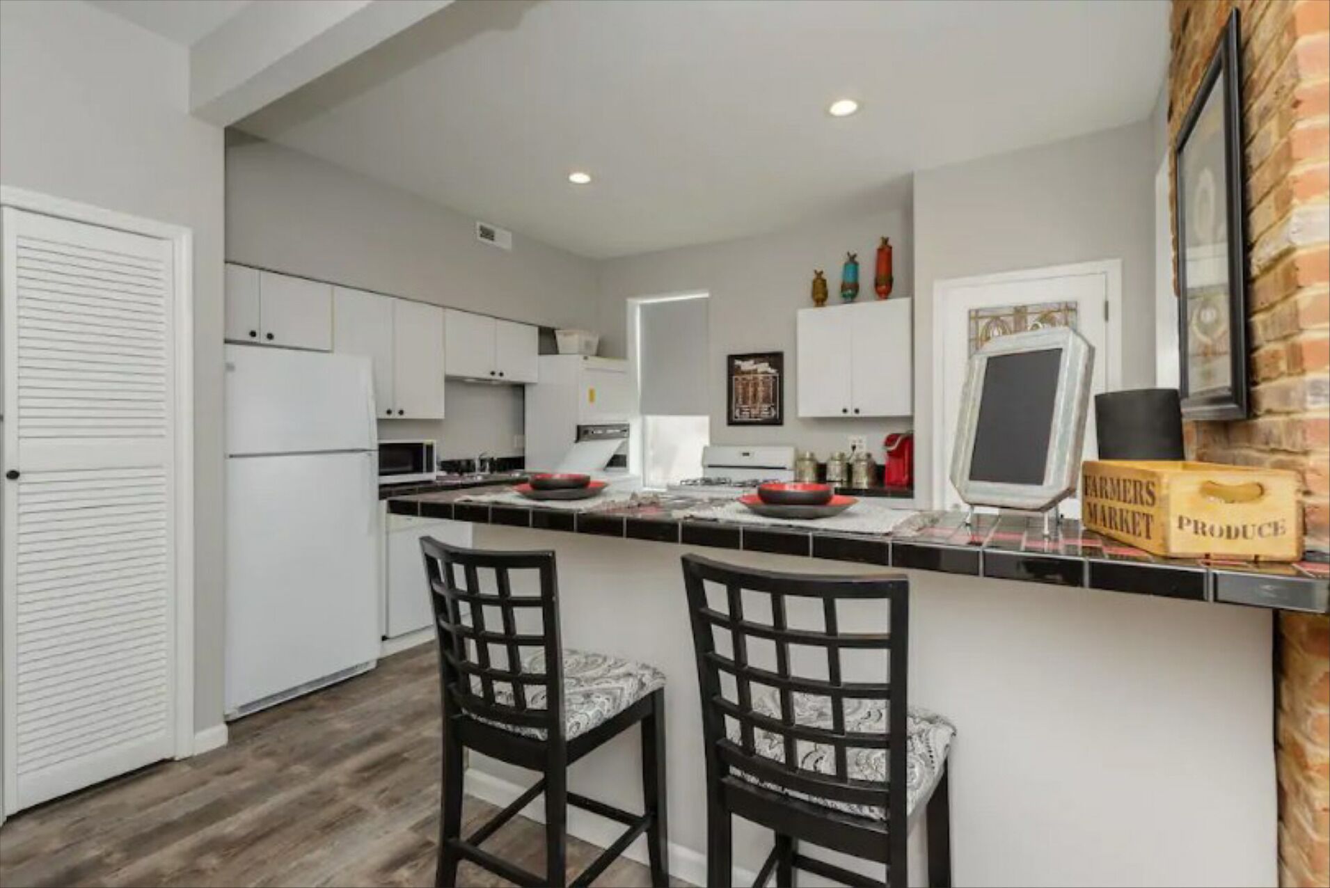 A modern kitchen with white cabinets, a black countertop, and two black chairs with marble upholstery.