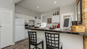 A modern kitchen with white cabinets, a black countertop, and two black chairs with marble upholstery.
