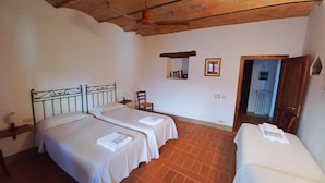 Quarto com duas camas, teto de madeira, parede de tijolos e uma janela pequena.