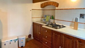 Uma cozinha com armários de madeira, fogão a gás, pia e painel de azulejos. Há lixeiras e um porta-utensílios de madeira na bancada.