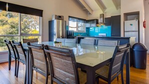 A modern kitchen with a central island, large windows, and a dining area with chairs. - Raywood - sleeps up to 17 (COWES)