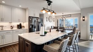 A modern kitchen with white cabinetry, a large island, and a dining area with wicker chairs. - High Heaven Mountain top dream (Sapphire)