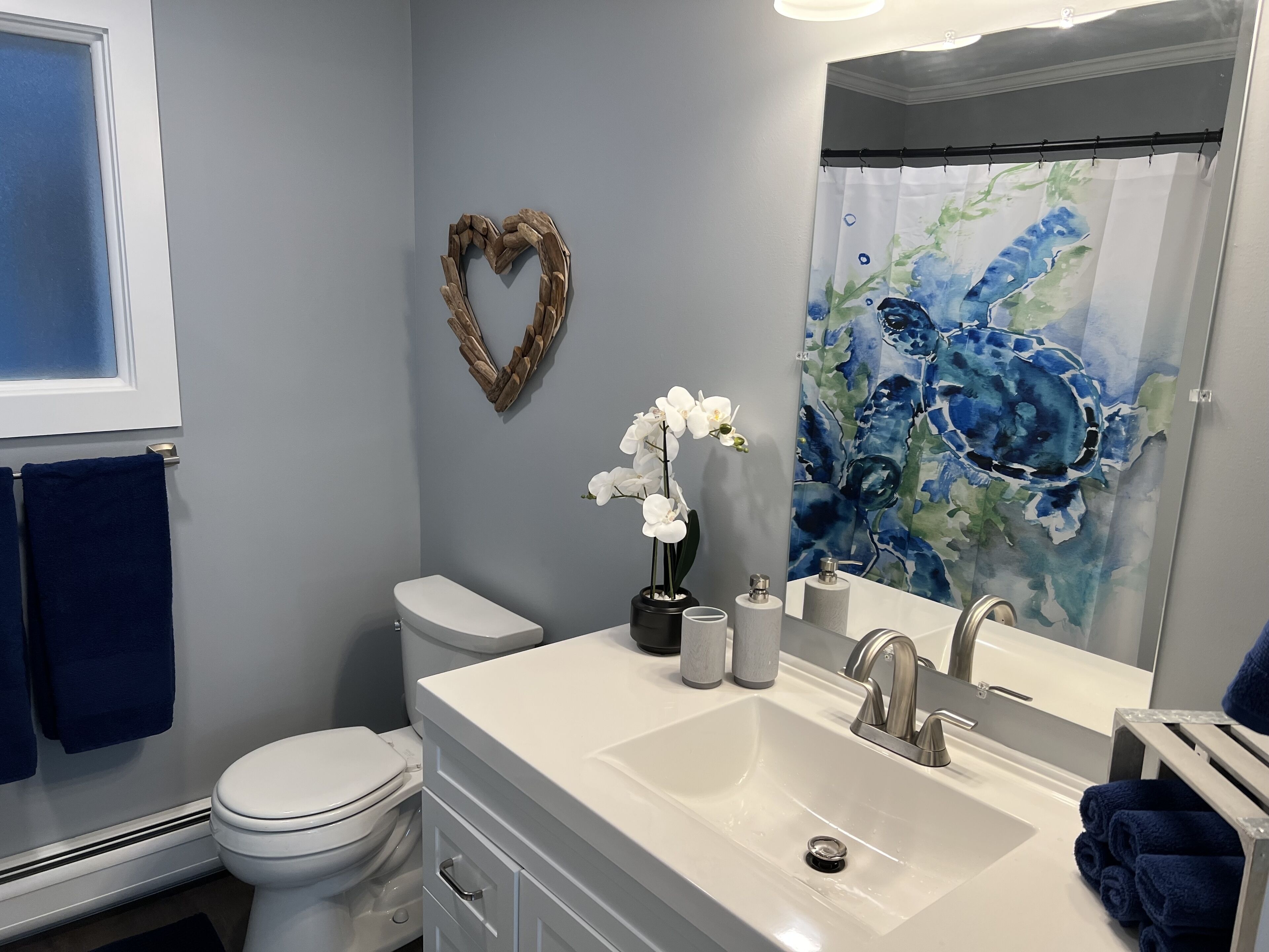 A bathroom with a white toilet, a sink with a mirror, a heart-shaped decoration on the wall, and a blue shower curtain.