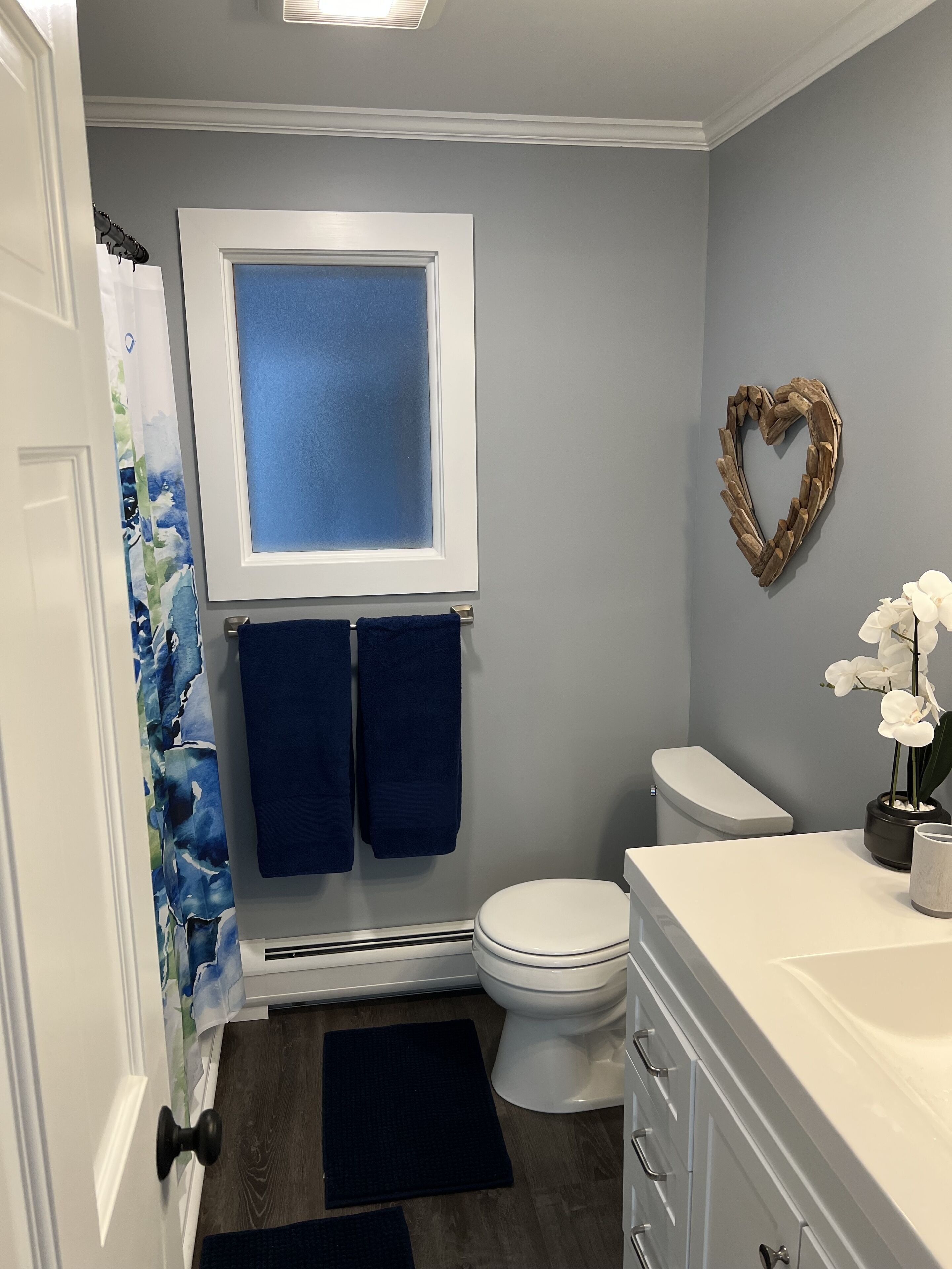 Een badkamer met toilet, douchegordijn, handdoekhouder, een hartvormige decoratie en een potorkidee.
