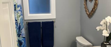Een badkamer met toilet, douchegordijn, handdoekhouder, een hartvormige decoratie en een potorkidee.