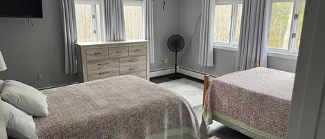 A bedroom with two beds, a ceiling fan, a dresser, and a window with curtains.