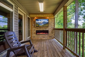 Enjoy a warm gathering by the fireplace on the deck, surrounded by lush greenery.