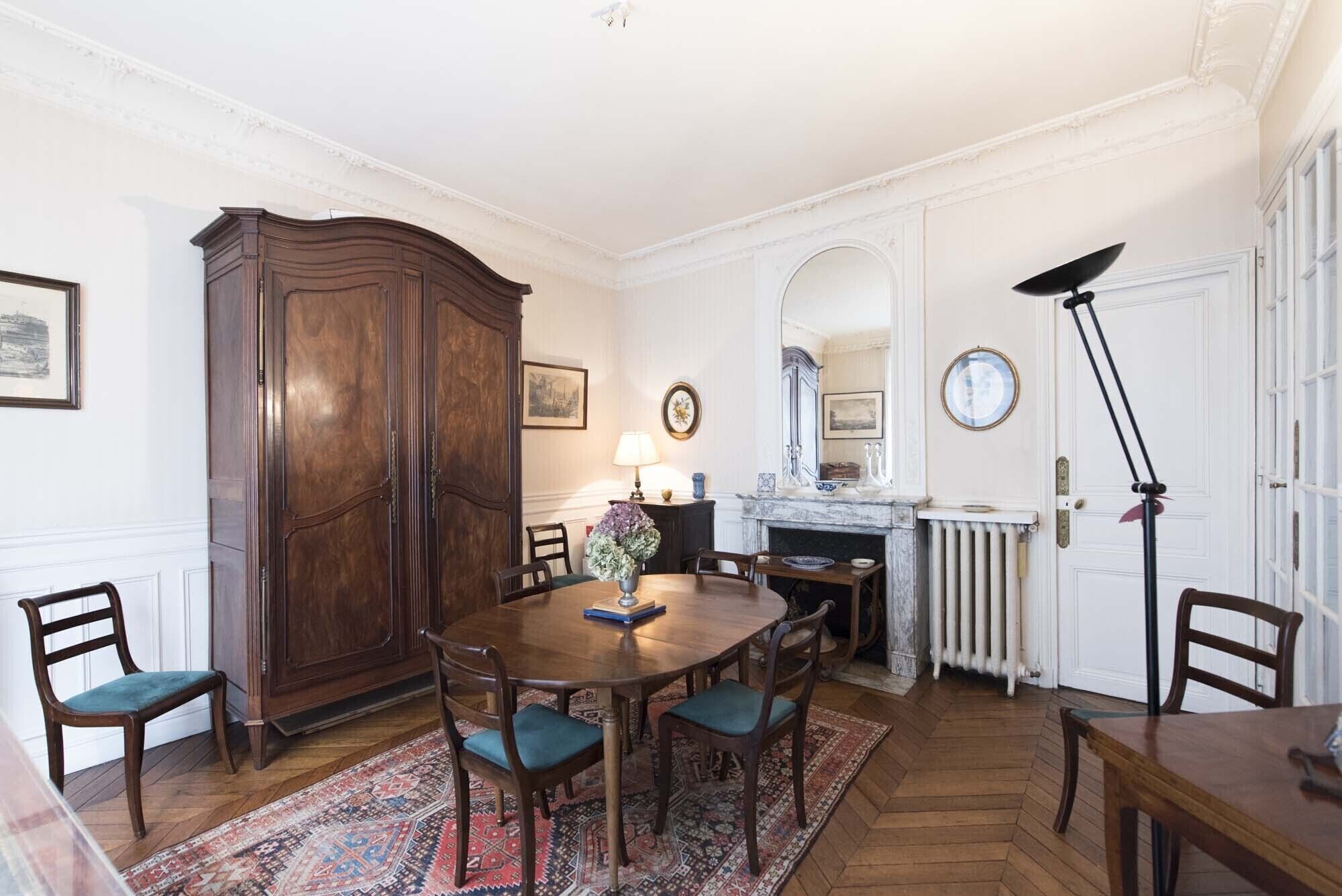 Une salle à manger avec une table en bois, des chaises, un grand buffet en bois, une cheminée et un radiateur.