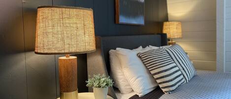 A bedroom with a bed, two bedside lamps, a small potted plant, and a framed picture on the wall.