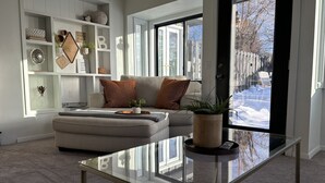 Ein modernes Wohnzimmer mit einem Glastisch, einem grauen Sofa und einem Bücherregal mit Dekoration.