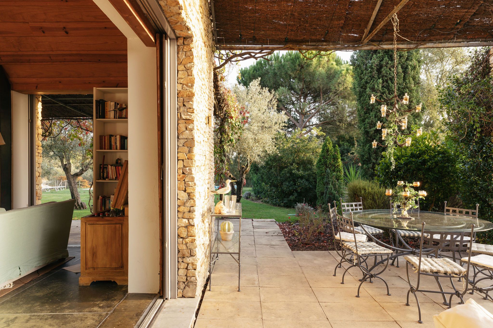 Een overdekte patio met een stenen muur, een glazen tafel met stoelen en een boekenkast.