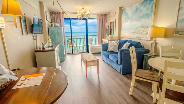 A room with a balcony, a dining table, a sofa, and a TV.