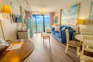 A room with a balcony, a dining table, a sofa, and a TV.