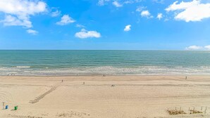 A beach with a clear sky, calm sea, and a few people walking.