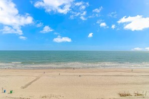 Une plage avec un ciel dégagé, une mer calme et quelques personnes qui se promènent.