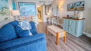 A living room with a blue sofa, a small table, a cabinet, and a beach-themed wall decoration.