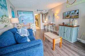 Un salon avec un canapé bleu, une petite table, un meuble et un élément de décoration murale sur le thème de la plage.