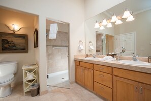 Ein Badezimmer mit Toilette, Waschbecken und Dusche. An der Wand hängt ein Bild und ein Mülleimer steht bereit.