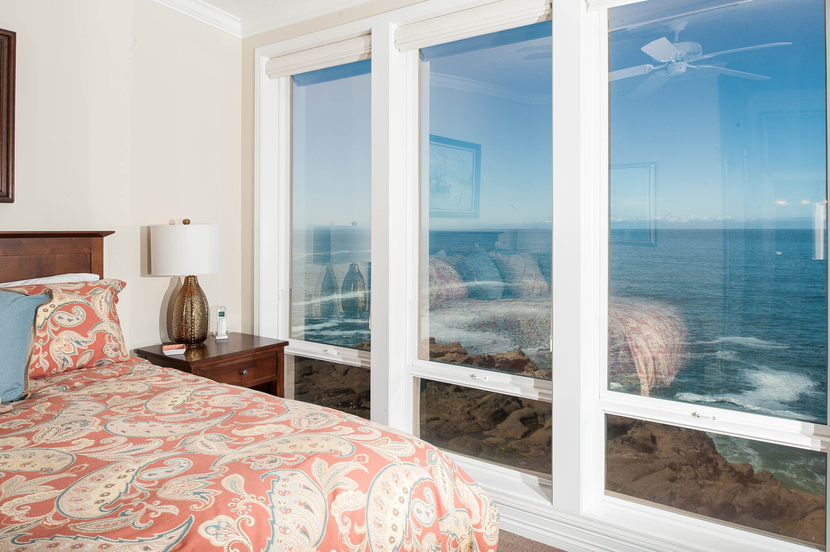 A bedroom with a large window overlooking a rocky coastline.