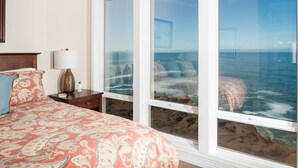 A bedroom with a large window overlooking a rocky coastline.