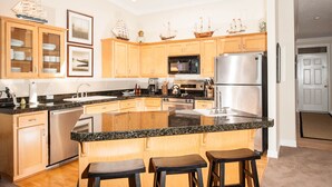 A modern kitchen with wooden cabinets, a large island with bar stools, stainless steel appliances, and decorative ship models on the wall.