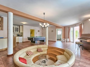 Uma sala de estar ampla com mesa de bilhar, sofás, mesa de jantar e um piano.