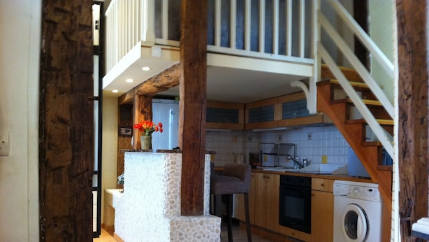 A kitchen with wooden cabinets, a washing machine, and a staircase leading to an upper level. - Unusual, Charming 16th Century Apt Near Place Des Vosges (Paris)